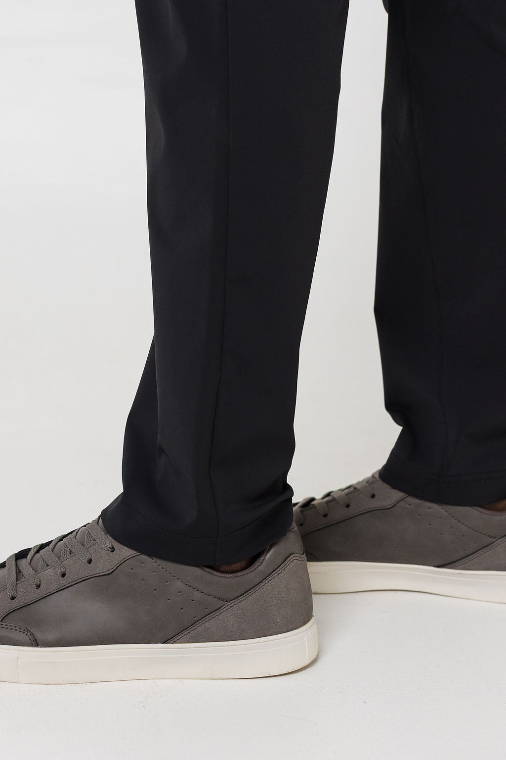 Person wearing black pants and gray sneakers on a light background