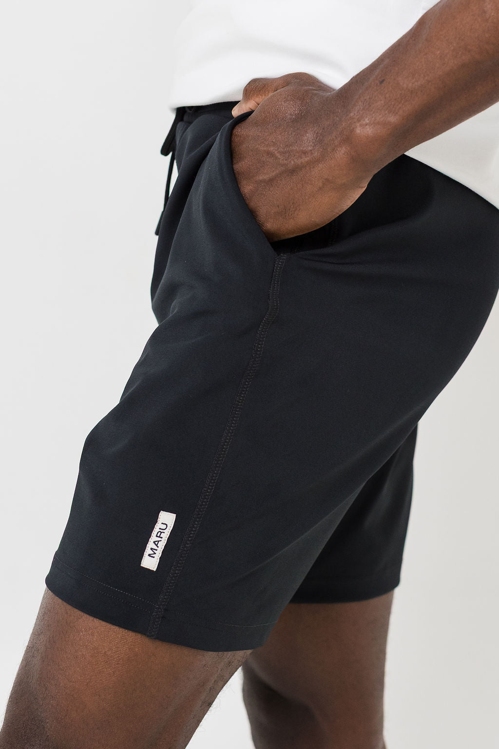 Man wearing black shorts and white t-shirt on a white background. Hands in pockets 