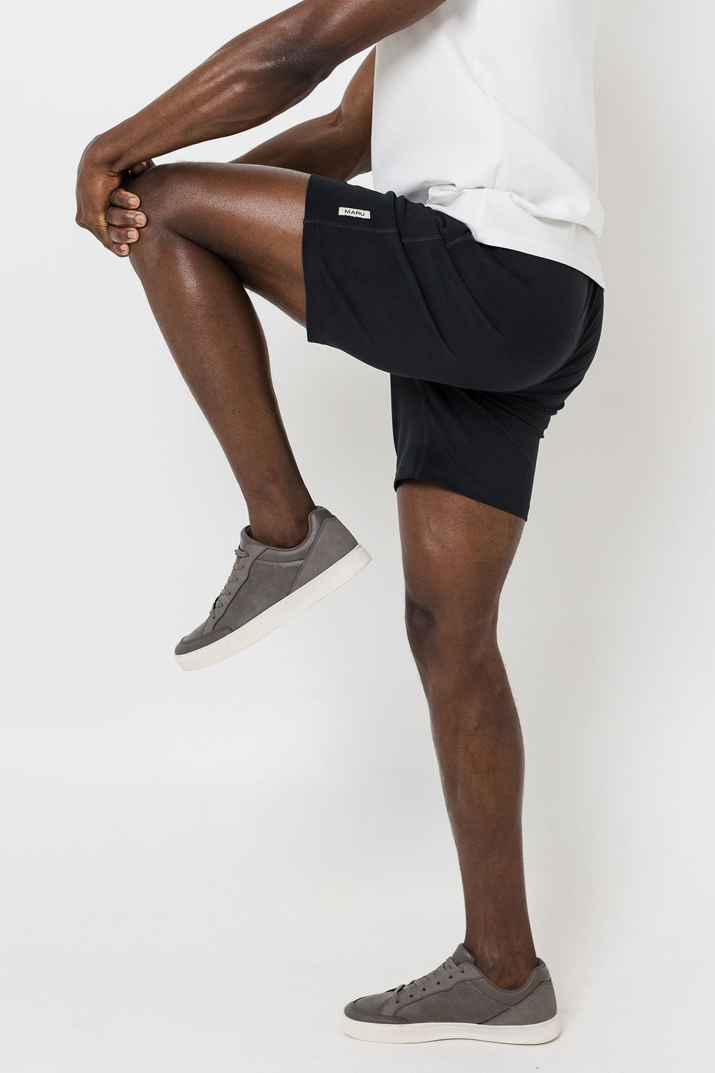 Man wearing black shorts and white t-shirt on a white background. Knee raised