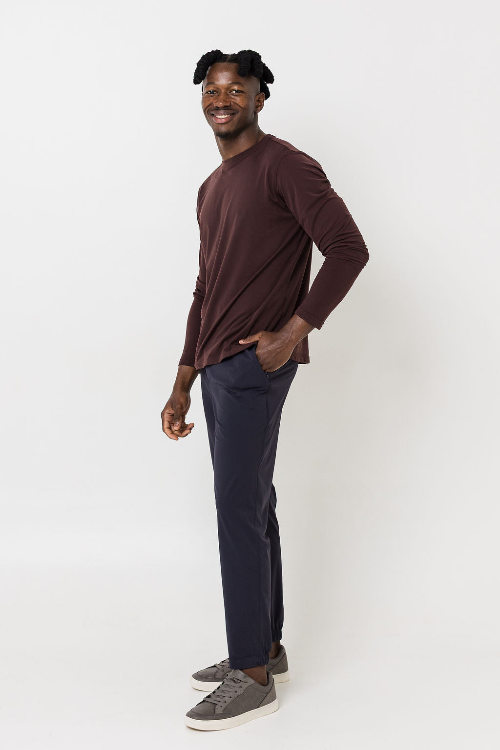 Man wearing a brown long-sleeve shirt and dark pants on a white background